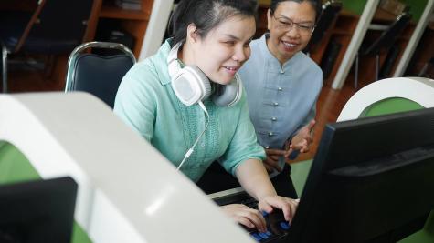 student with a disability working with at a computer with a peer