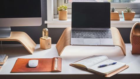 A home works set-up with a laptop, monitor, mouse, notebook and pen