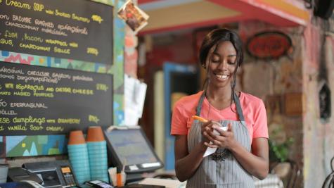 A worker wearing an apron and writing on a notepad standing behind the counter of a cafe. 