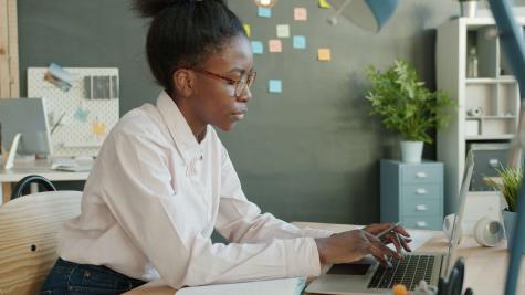 A person sitting at their laptop in front of a wall of sticky notes.