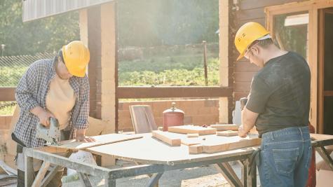Two construction workers working at a saw bench. They are wearing hard hats.