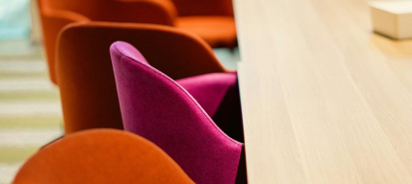 A series of chairs at a table. Orange chairs surround one singular pink chair.