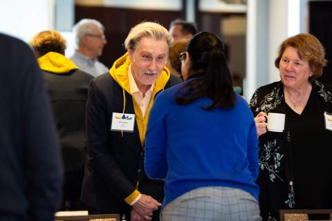 Three people greet each other. They are leaned into each other having a conversation