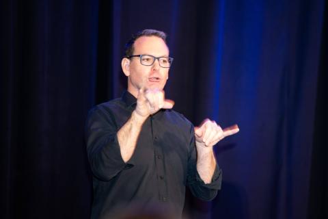 A sign language interpreter signs to the audience onstage in front of blue curtains