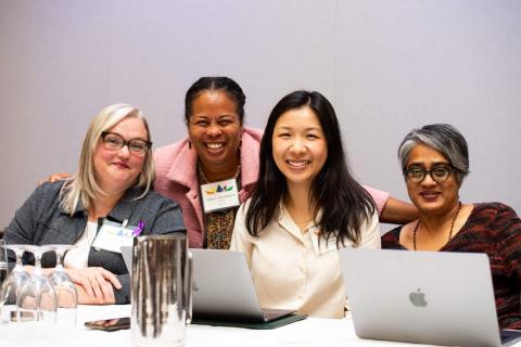 Four people take a picture together. Two of them have laptops in front of them and the other two have nametags on
