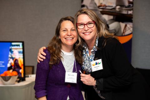 Two people wearing nametags embrace and pose for a photo, smiling at the camera