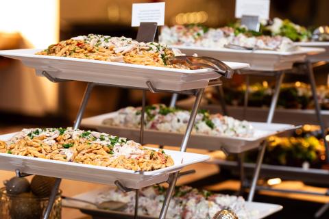 Catered food tables. Pasta dishes sit on trays displayed for people to self-serve