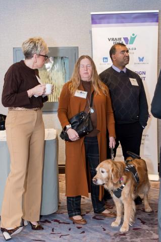 A group of people converse while a service dog stands by.