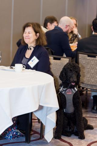 A person sits at a table with their service dog sitting close by
