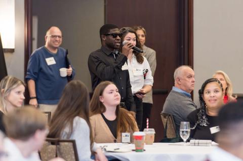A speaker holding a microphone standing in between tables 