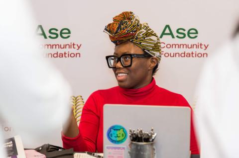 A person sits at a table with a laptop in front of them. They smile to someone off-camera.