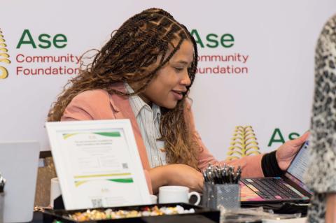 A person in front of an A.S.E Community Foundation banner on their laptop.