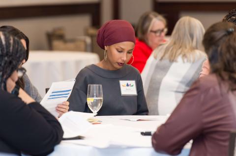 Four people sit at a table with water glasses and paperwork.