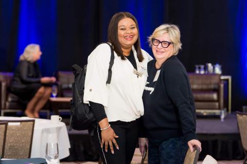 Two people pose and smile for a photo in front of the stage and its' blue curtain.