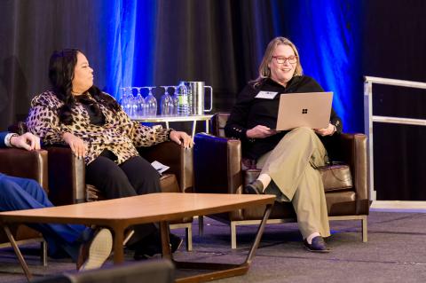 Three speakers sit on stage. One has a laptop balanced on their lap.