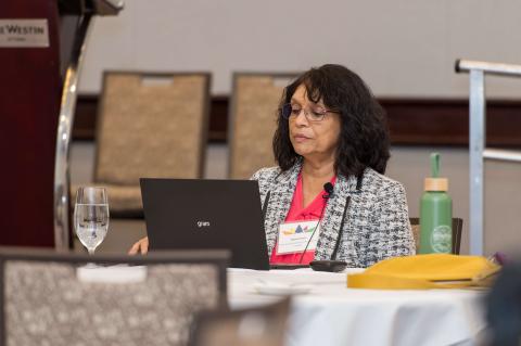 A person sits at a table in front of a laptop and some water glasses.