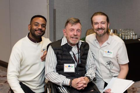 Three people pose for a picture. They stand shoulder to shoulder and smile at the camera.