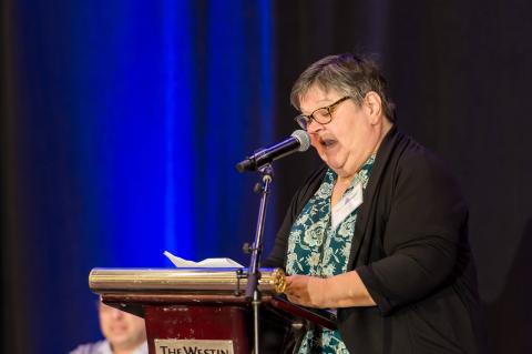 A speaker talks into a microphone. They read off of a page and stand at a podium.