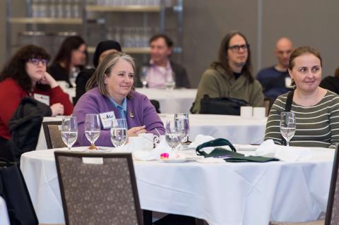 Several tables of guests stare ahead at the stage.