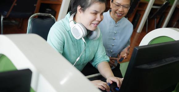 student with a disability working with at a computer with a peer