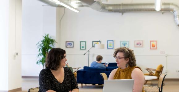 Two people sit at a table in front of a laptop.