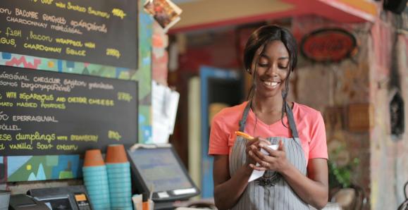 A worker wearing an apron and writing on a notepad standing behind the counter of a cafe. 